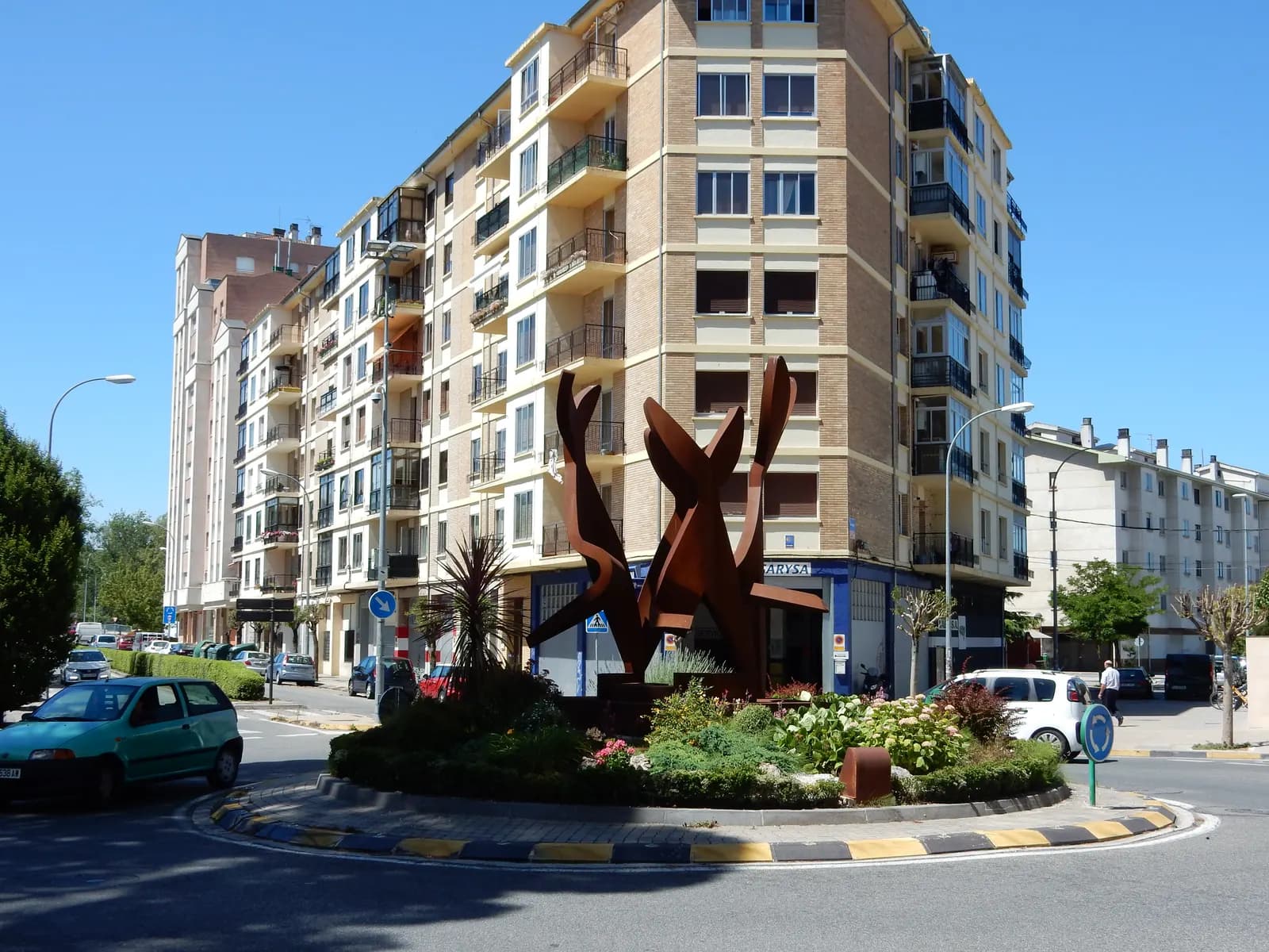 Rotonda con una escultura de hierro oxidado en Burlada, rodeada de bloques de viviendas de seis y siete plantas