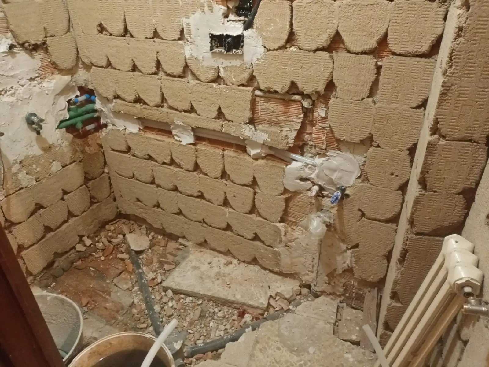 Baño demolido con paredes de ladrillo, escombros y tuberías de agua a la vista
