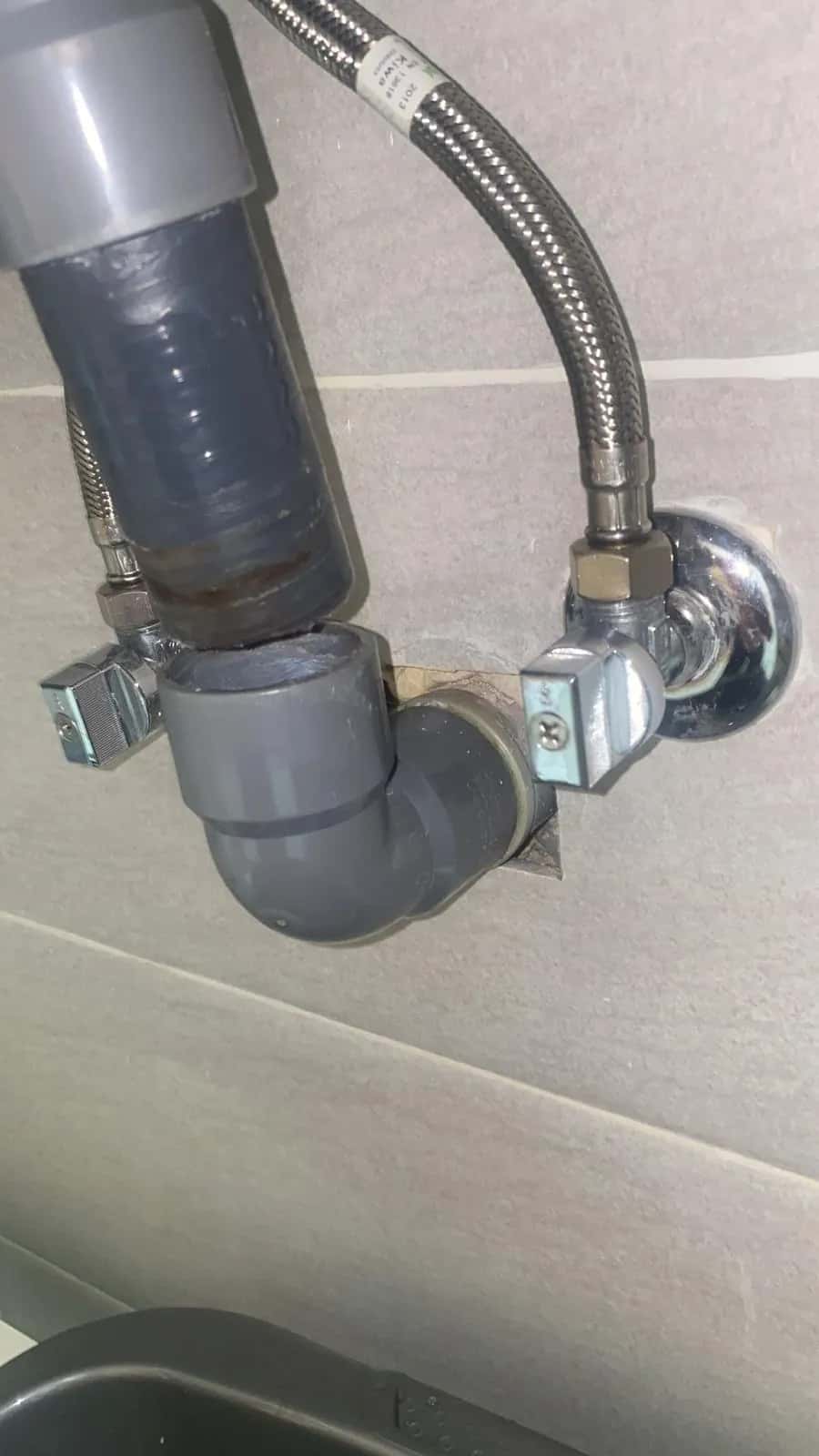 Desagüe de PVC gris y llave de escuadra con latiguillo bajo un lavabo