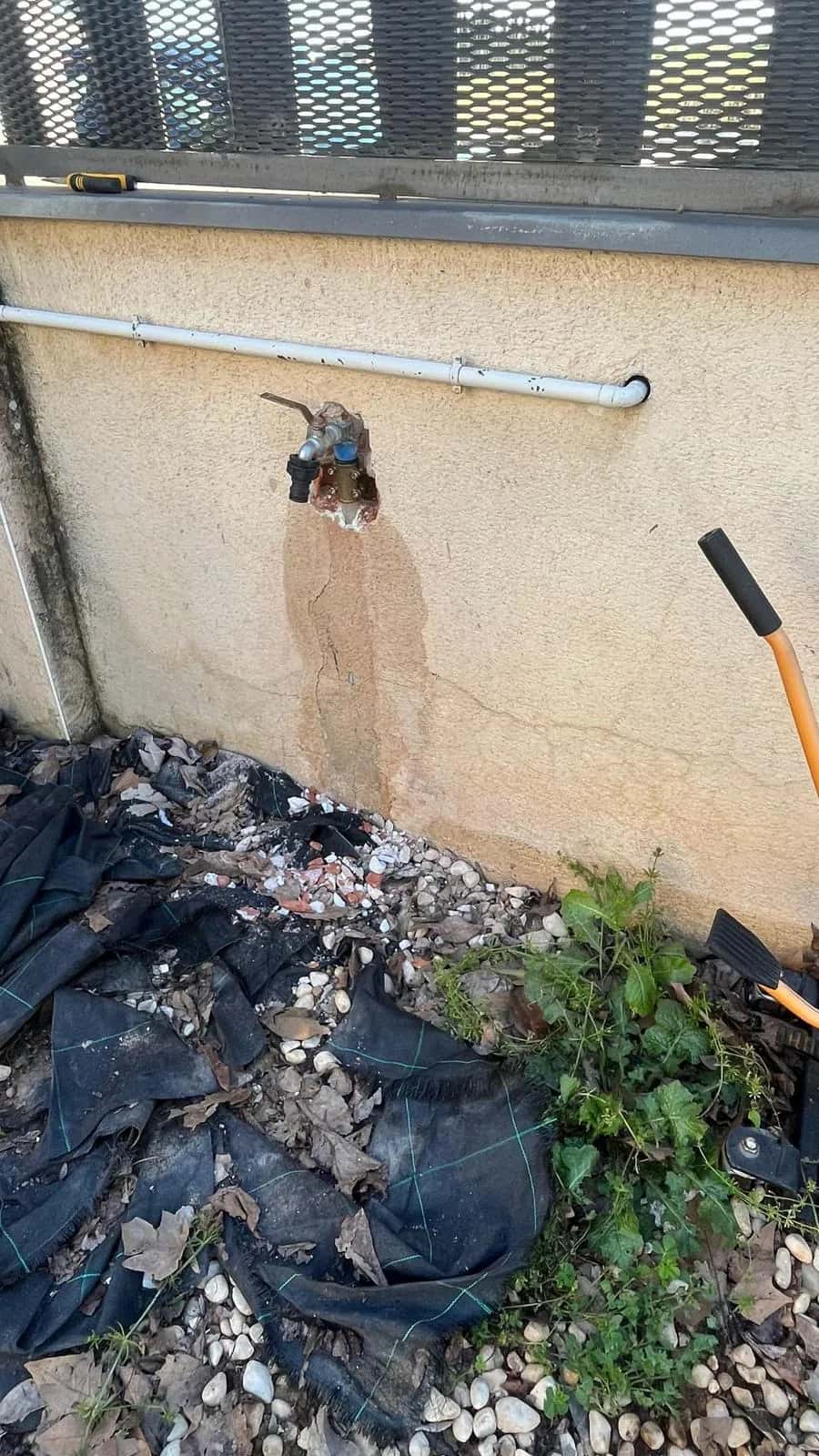 Grifo exterior con mancha de humedad en la fachada sobre un jardín