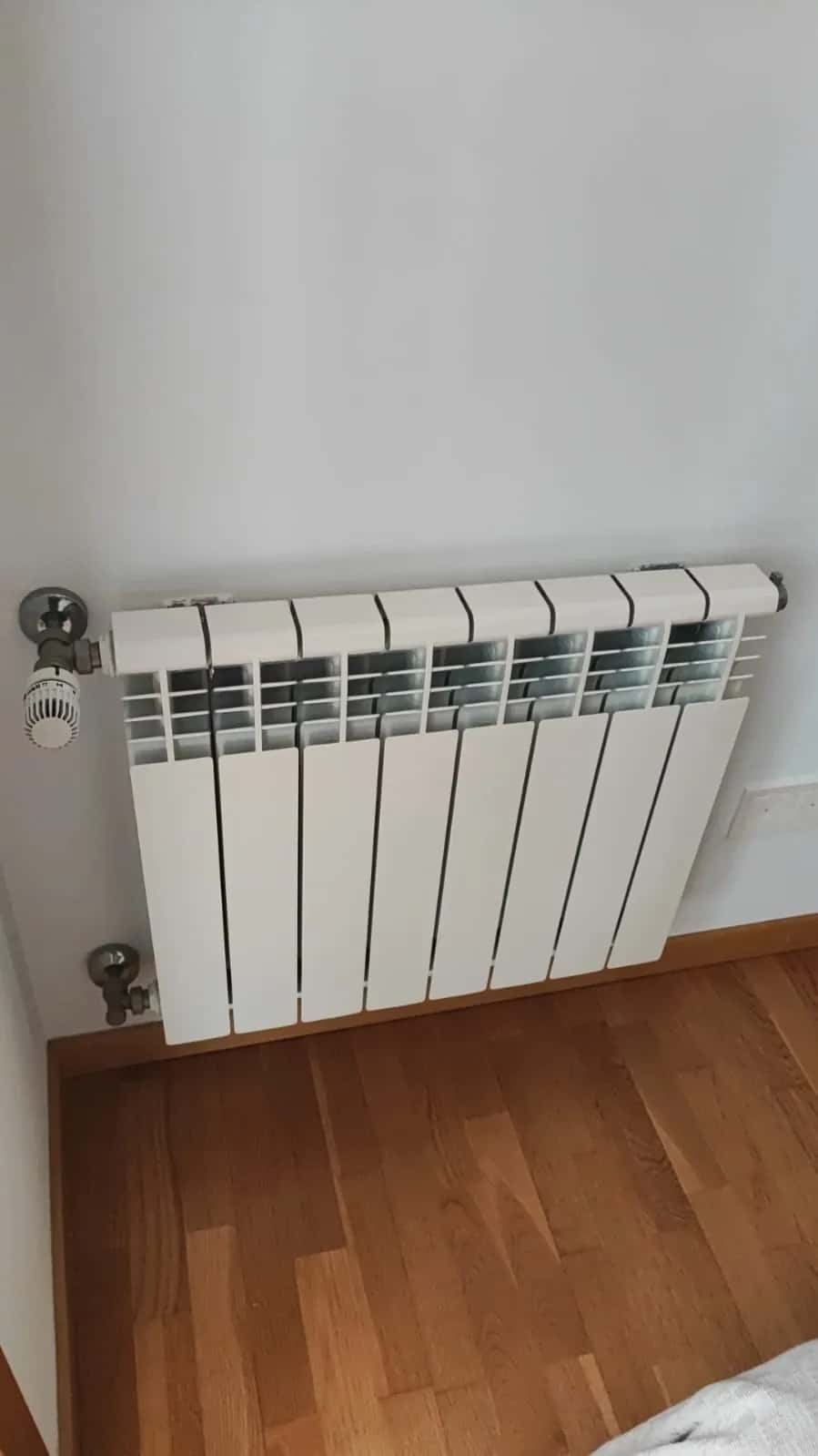 Radiador de aluminio con válvula termostática instalado sobre suelo de tarima
