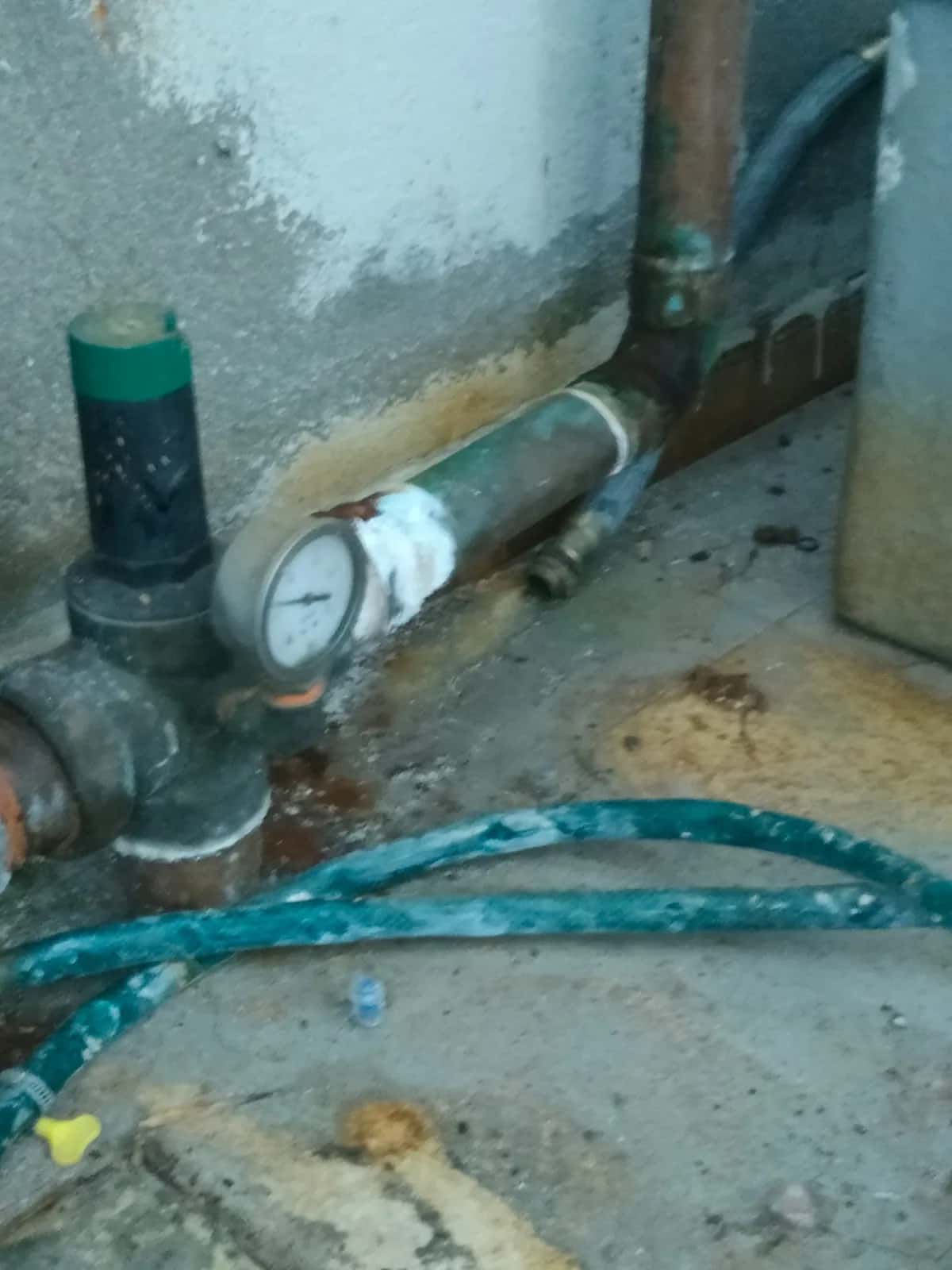 Tubería corroída con manómetro y restos de humedad en el suelo