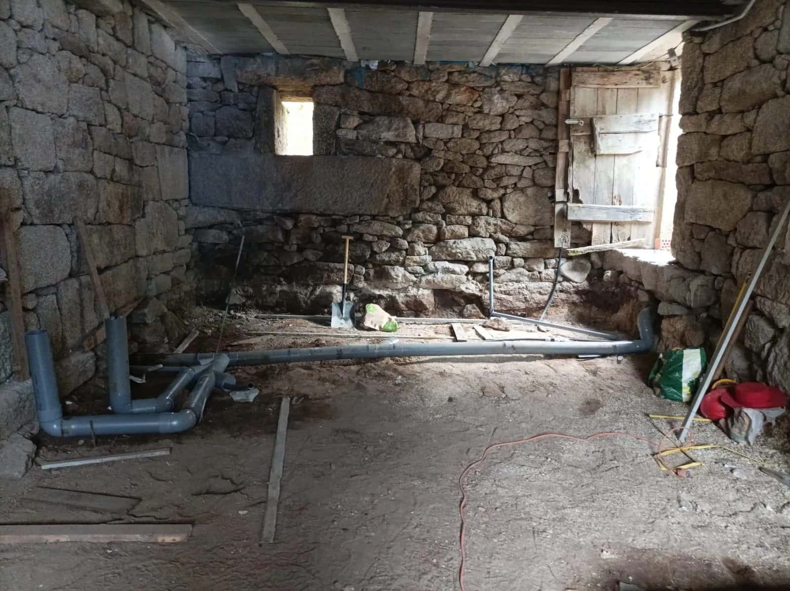 Tuberías de desagüe de PVC colocadas sobre el suelo de tierra de una casa de piedra en rehabilitación